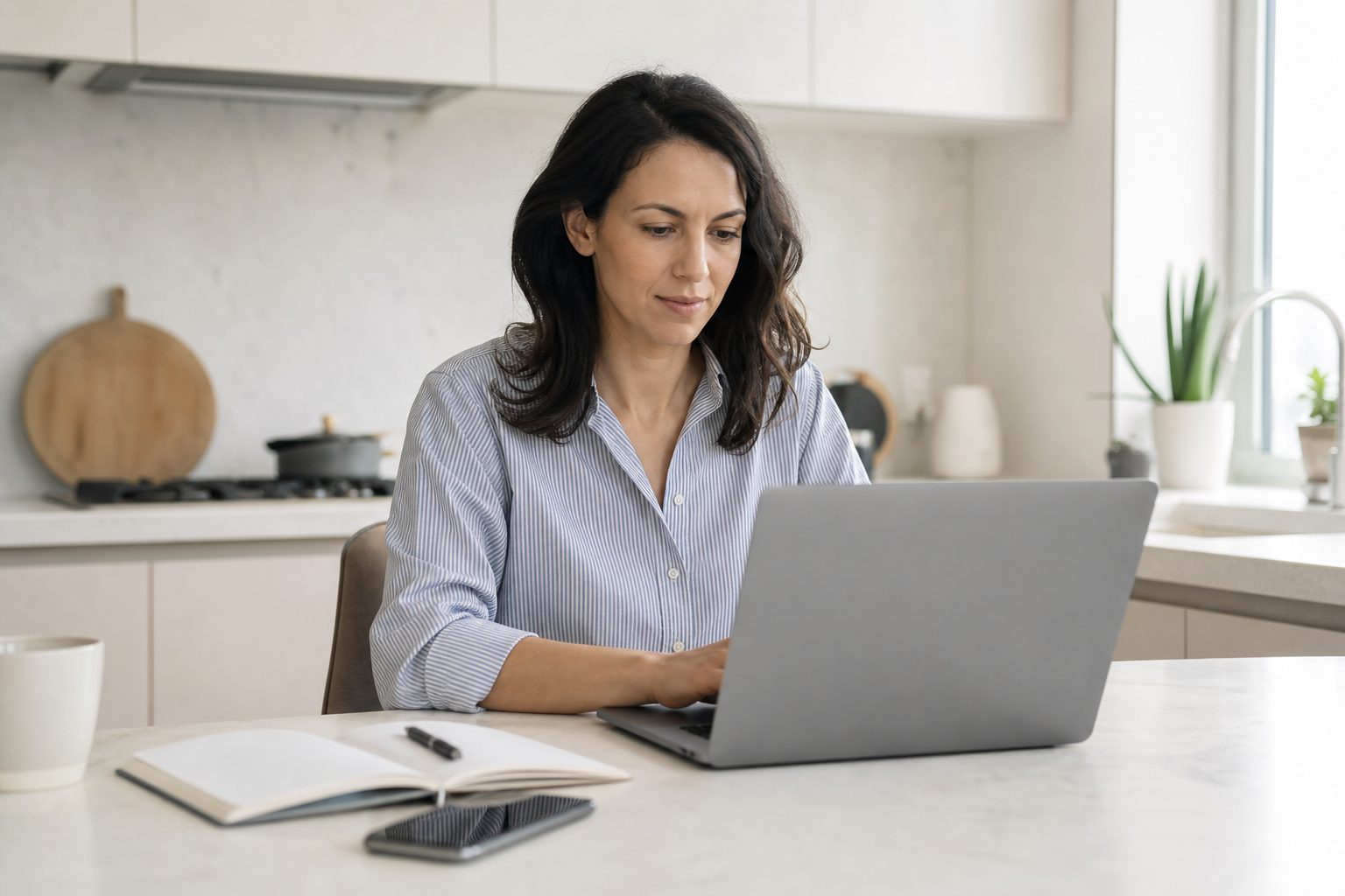 Chapter treasurer reviewing payments on a phone and laptop at a bright kitchen table