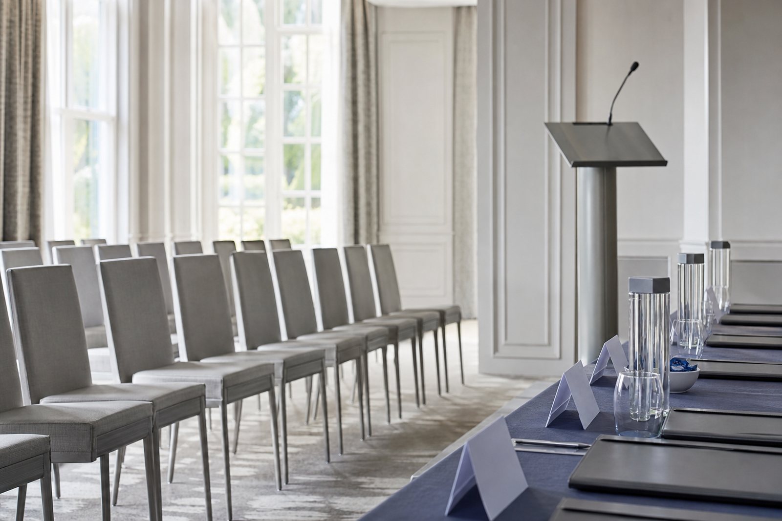 A bright meeting room set with chairs, a lectern and a table holding folders and name card holders in soft daylight